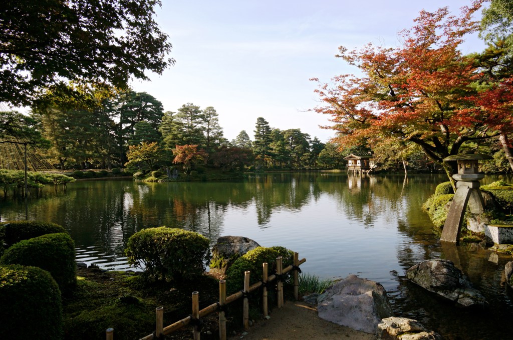 Kenrokuen pond with red autumn maples, pines, and a stone lantern in Kanazawa, Japan