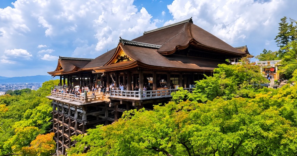 The Main Hall and wooden stage of Kiyomizu-dera in Kyoto, standing on tall pillars above a green hillside