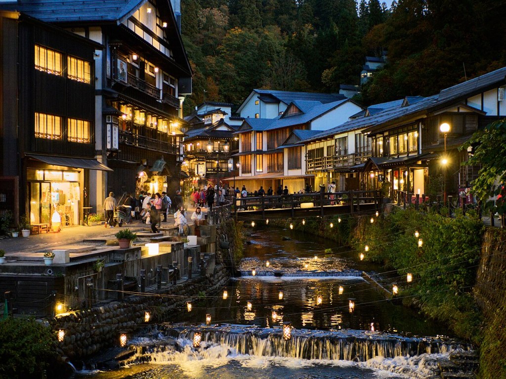 Illuminated wooden ryokan lining the river in Ginzan Onsen at blue hour